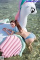 A woman in a bikini laying on an inflatable unicorn in the water.