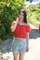 A woman in a red top and denim shorts posing for a picture.