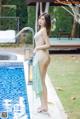 A woman in a white bikini standing next to a swimming pool.