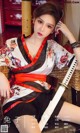 A woman in a kimono sitting on a chair holding a sword.