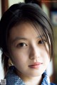 A young woman in a blue and white kimono looks at the camera.