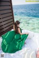 A woman in a green dress sitting on a bed by the ocean.